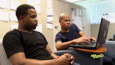 Two young men working on a laptop in an office.