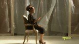 A woman sitting on a chair in front of a curtain.