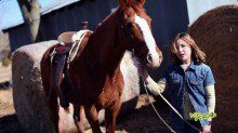 A girl in blue denim jacket holding horse rope