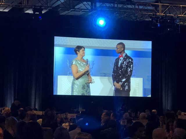 A man and woman standing in front of a large screen.