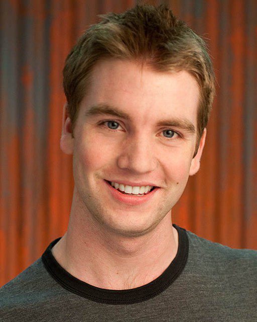 A young man smiling in front of an orange wall.