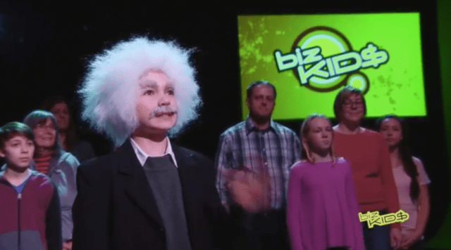 A man in a white wig is standing in front of a green screen.