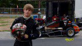 A young man in a race car holding a helmet.