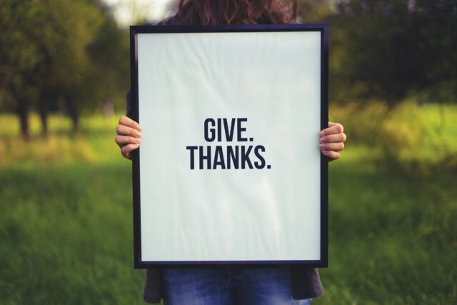 A Woman Holding a Poster of Give. Thanks.